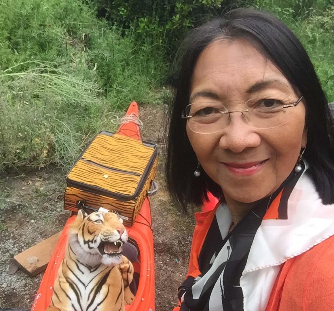 Elaine Chan headshot with a stuffed tiger in an orange kayak behind her