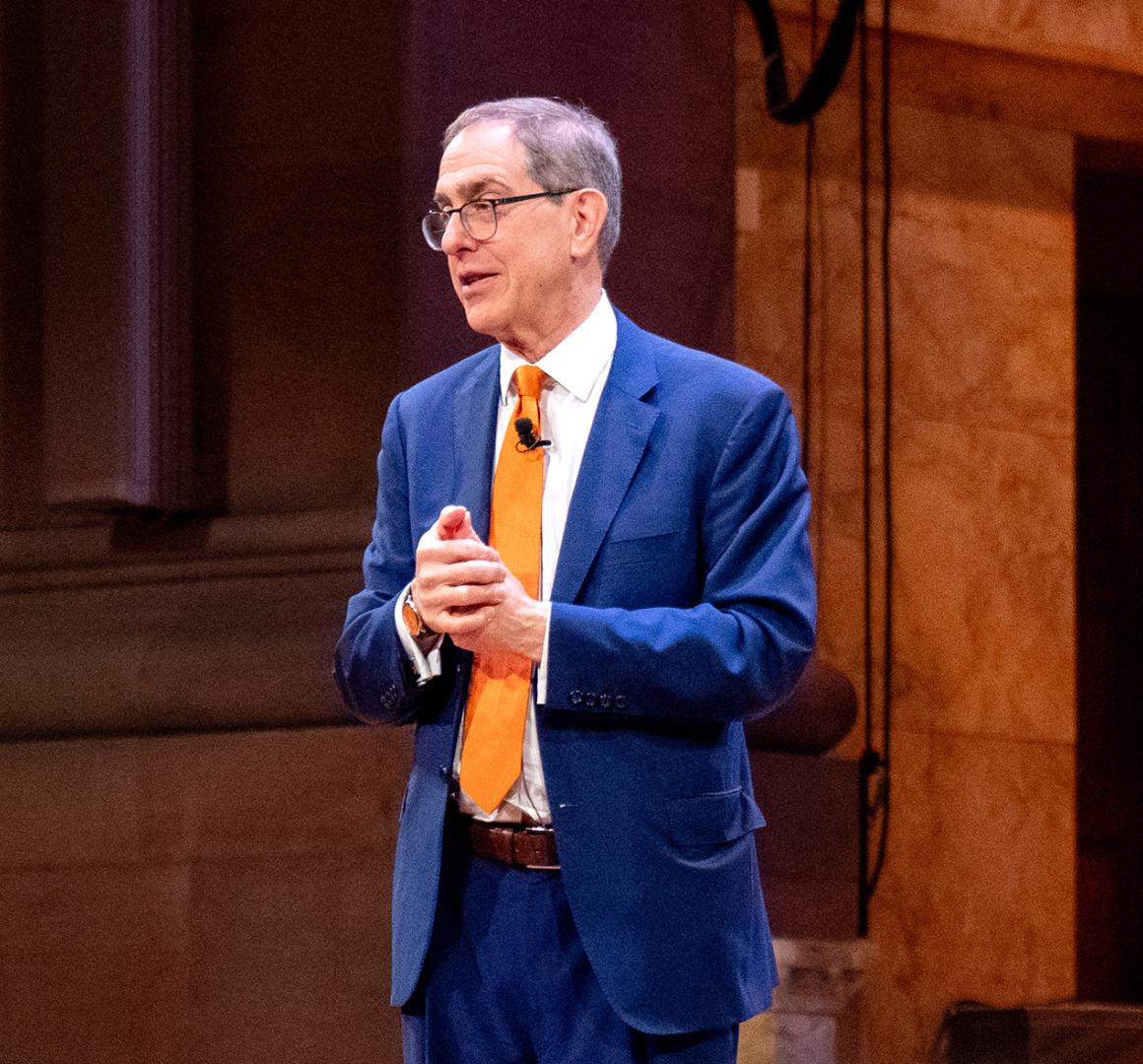 President Eisgruber, wearing a blue suit, speaking on the stage of Richardson Auditorium