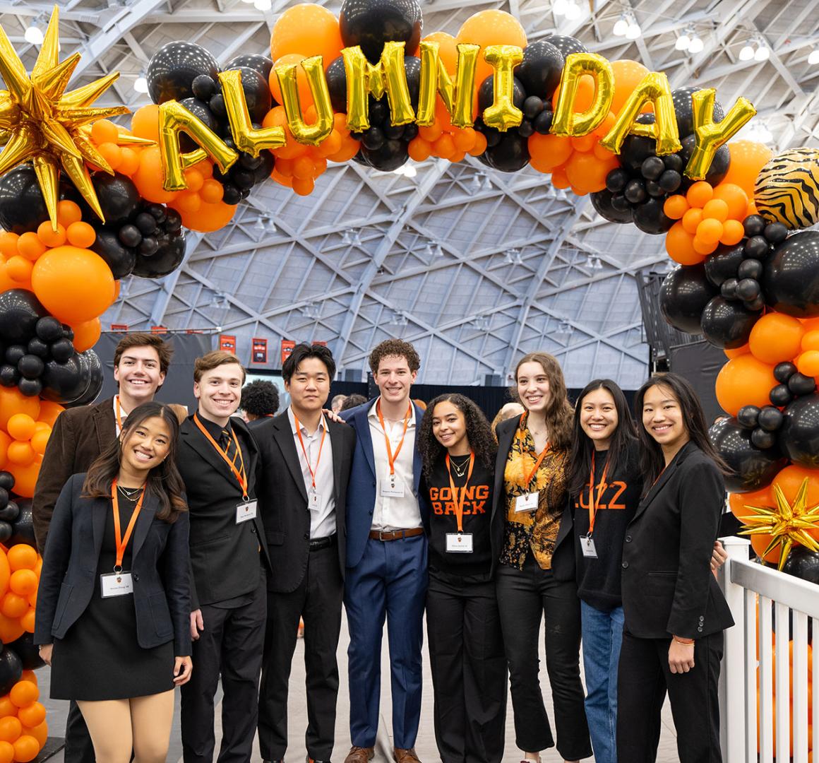 A group of alumni stand under a balloon arch