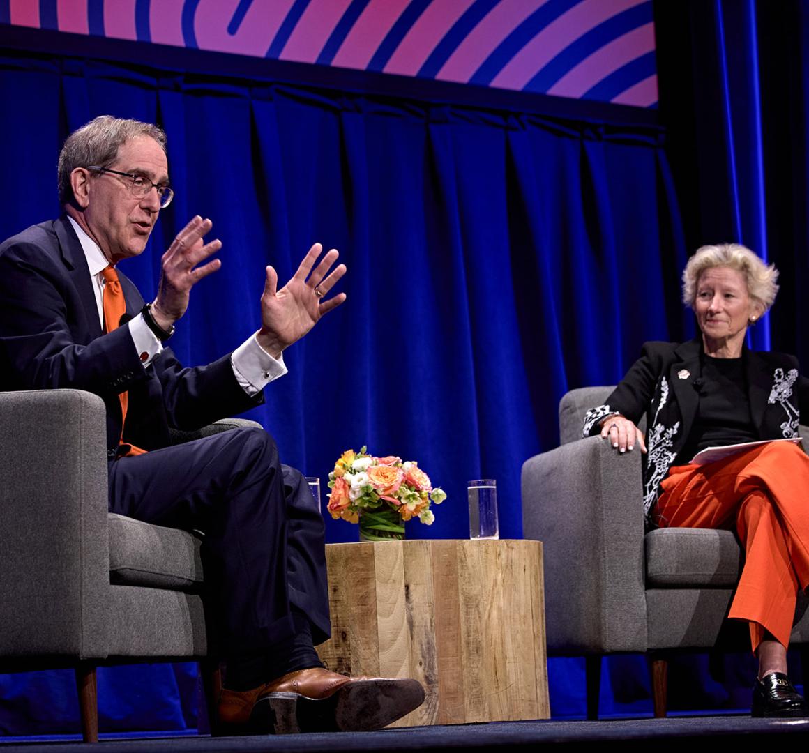 President Eisgruber, seated on stage alongside Weezie Sams, speaking to a packed hall.