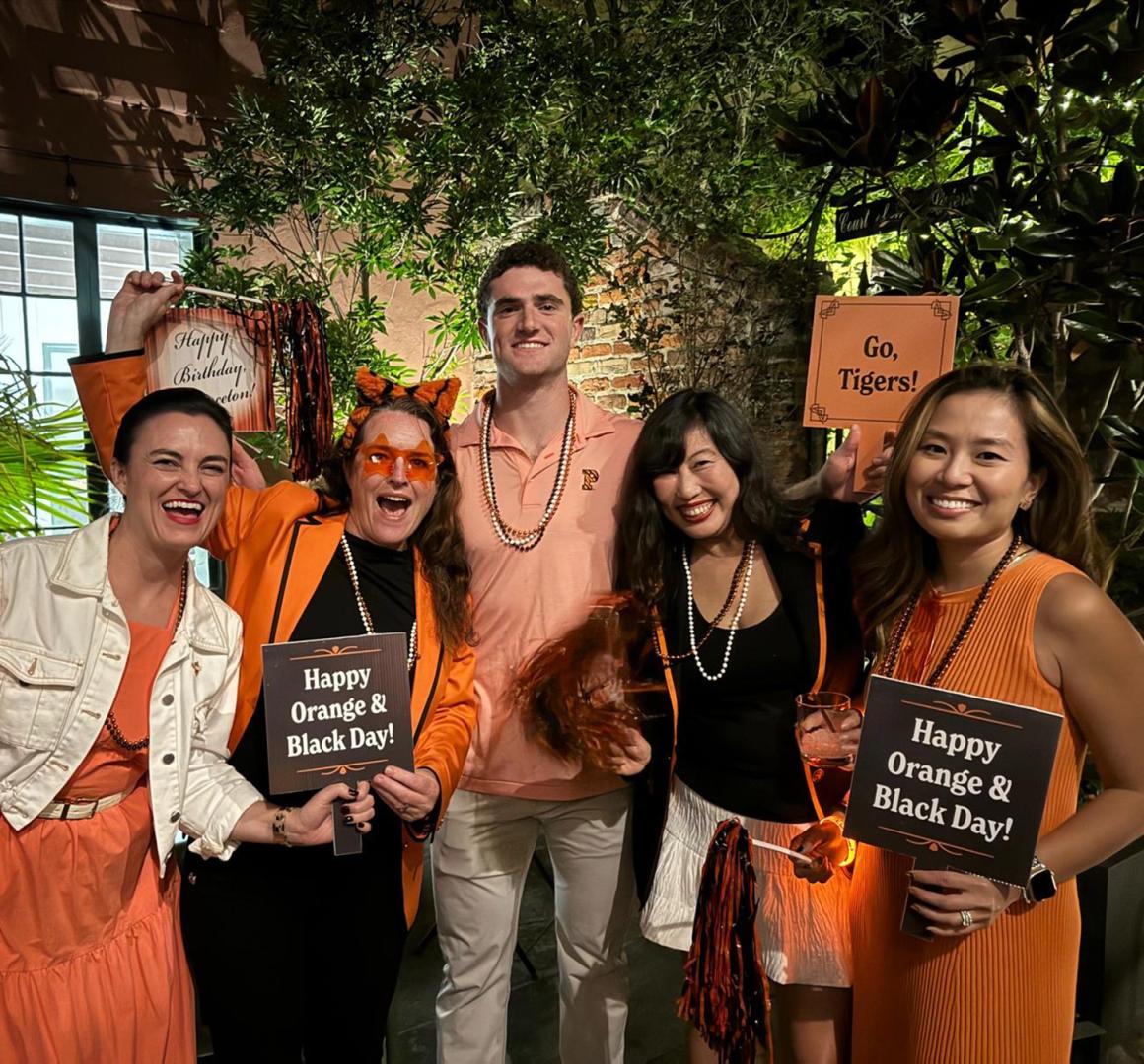 Five orange-clad alums proudly displaying Orange & Black Day signs