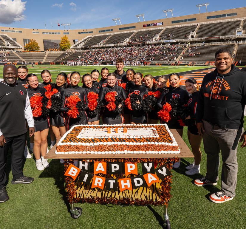 John Mack, Erik Plummer and the Princeton cheerleaders huddle around an orange birthday cake in Princeton Stadium