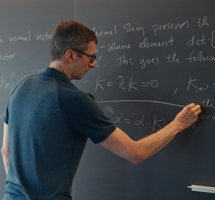 A male professor calculates advanced math equations on a classroom chalkboard.