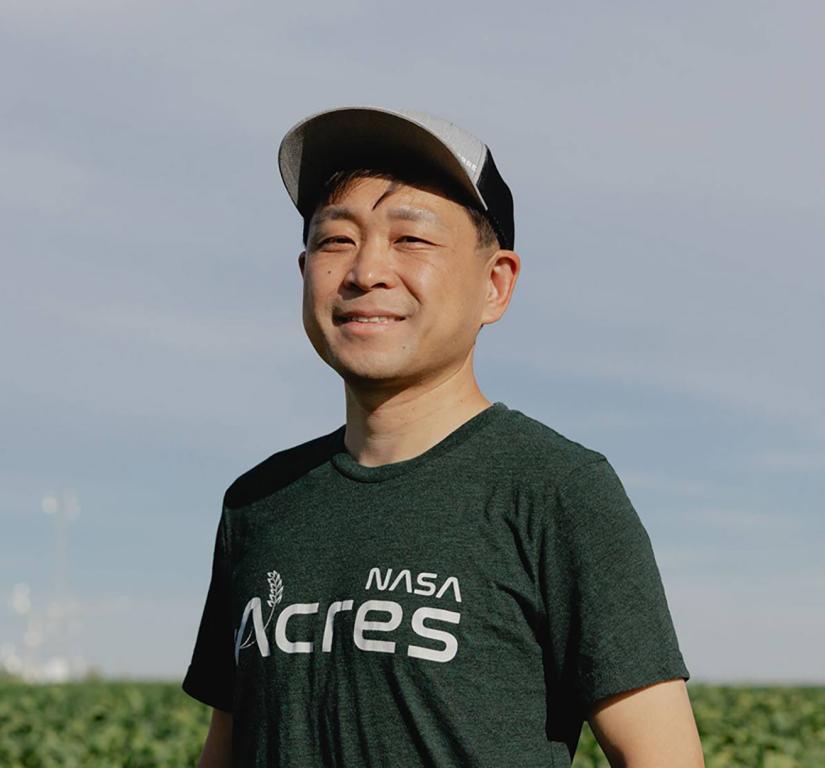 Asian male in baseball hat, standing in a farm field surrounded by green crops