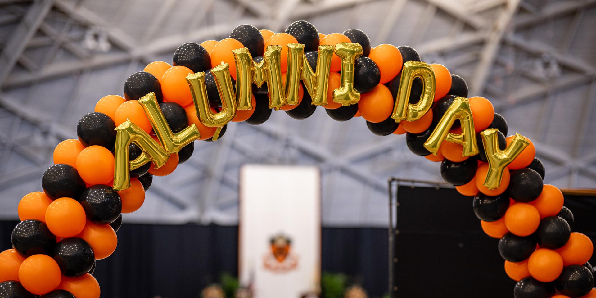 Orange and black balloons, decorated with golden letters that spell out Alumni Day in Jadwin Gymnasium
