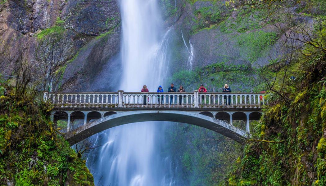 Multnomah Falls Bridge with a few people standing on the bridge and waterfall behind the bridge