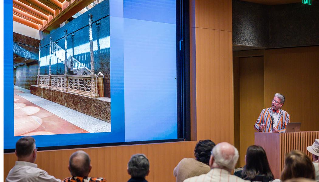 James Steward at a podium with a photo of the interior of the art museum on the screen to his left