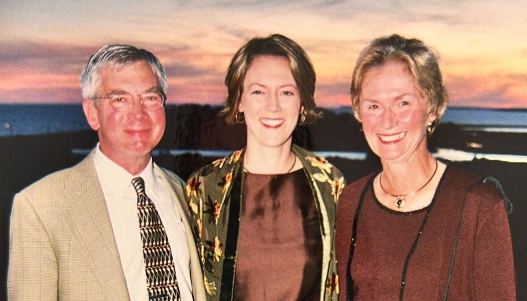 Three people stand together in front of a sky at sunset