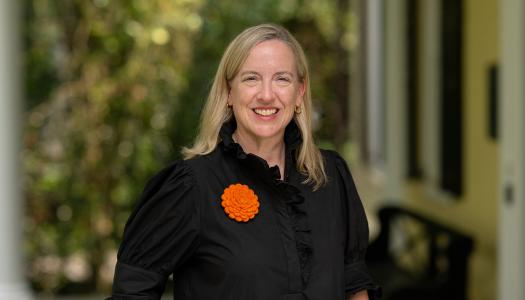 Jennifer Caputo, dressed in black and orange, standing on the porch of Maclean House