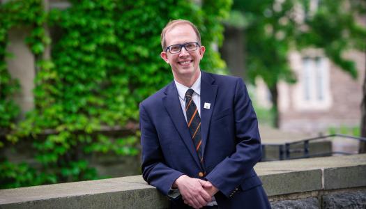 Andrew Houck, wearing a jacket and Princeton tie, stands in front of an ivy-covered building