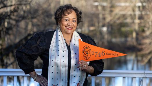 Juanita James, smiling, hand on hip, holding an orange 1746 Society pennant