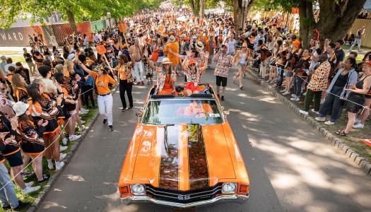 An orange convertible with black stripes is cheered by bystanders in the P-rade