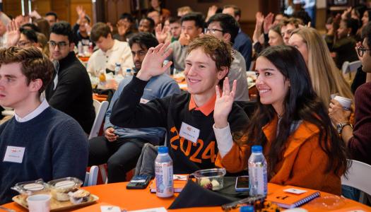 Recent alumni seated in Chancellor Green raise their hands to volunteer