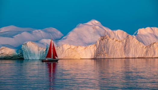 A boat sailing in front of a giant iceberg