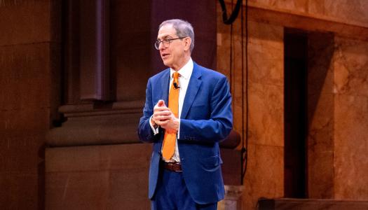 President Eisgruber, wearing a blue suit, speaking on the stage of Richardson Auditorium