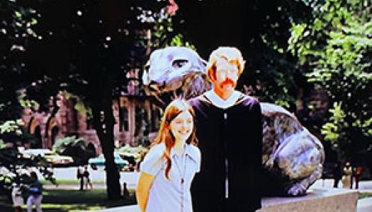 Bonnie Hewson and Chuck Marboe in front of a tiger statue; he is wearing a graduation gown