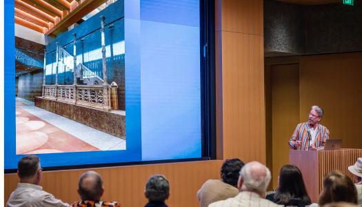 James Steward at a podium with a photo of the interior of the art museum on the screen to his left