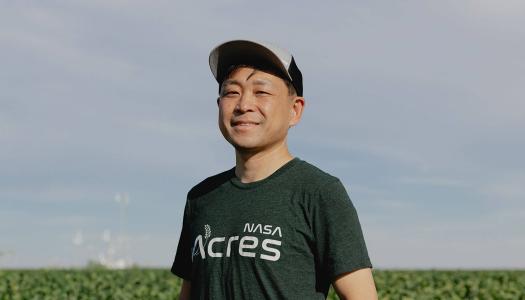 Asian male in baseball hat, standing in a farm field surrounded by green crops