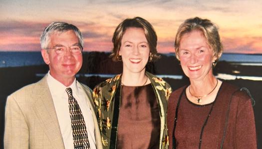 Three people stand together in front of a sky at sunset