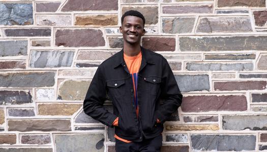 Godwin Obi, smiling and standing in front of stone exterior of academic building. 