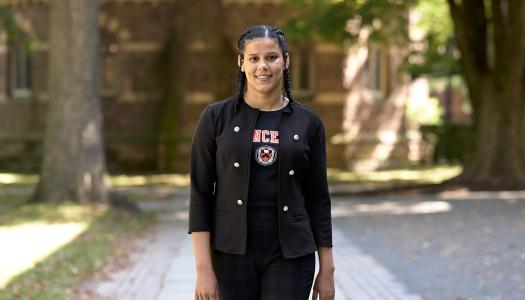 A smiling Princeton student walking near Nassau Hall. 