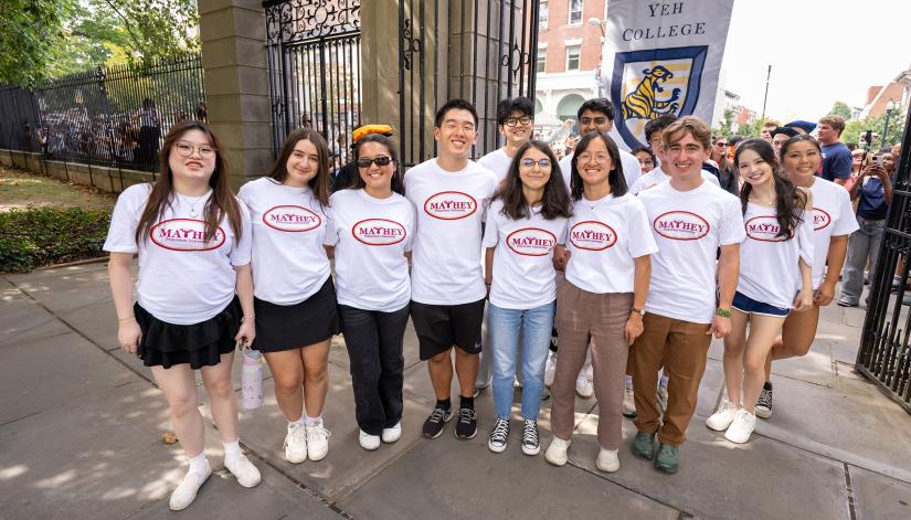 A group of new Princeton students wearing Mathey College white t-shirts pose together on the campus side of FitzRandolph Gate
