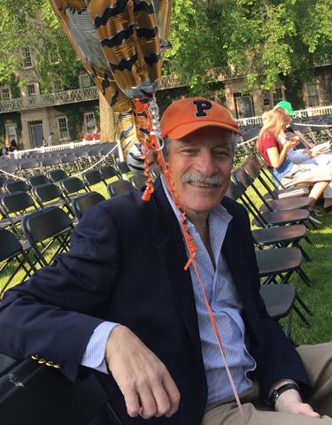 Male alumnus with orange Princeton baseball sitting on bench. 