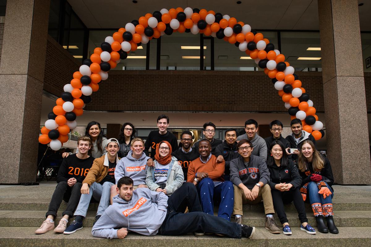 Group of alumni sitting below orange ballooon arch