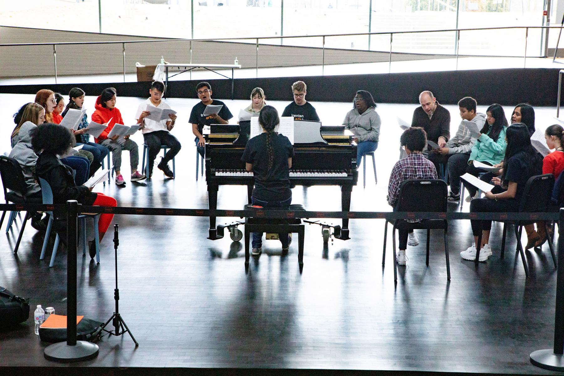 Trenton students sing together around a piano at the Lewis Arts complex.