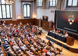 A gathering of alumni are gathered facing a panel in a classroom