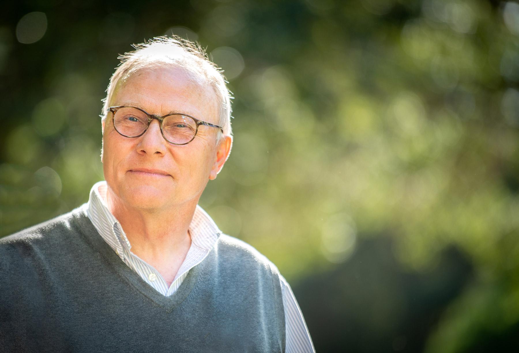 Sunny portrait of David Card outside standing in front of green trees