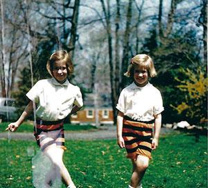 Two young girls on a lawn in white tops and orange and black striped shorts