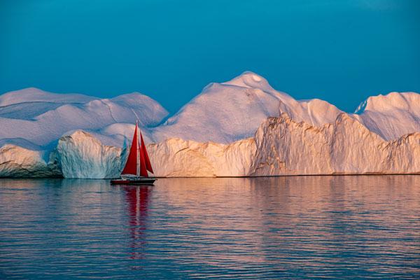 A boat sailing in front of a giant iceberg