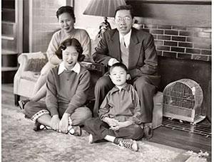 A family of four sits in front of a fireplace