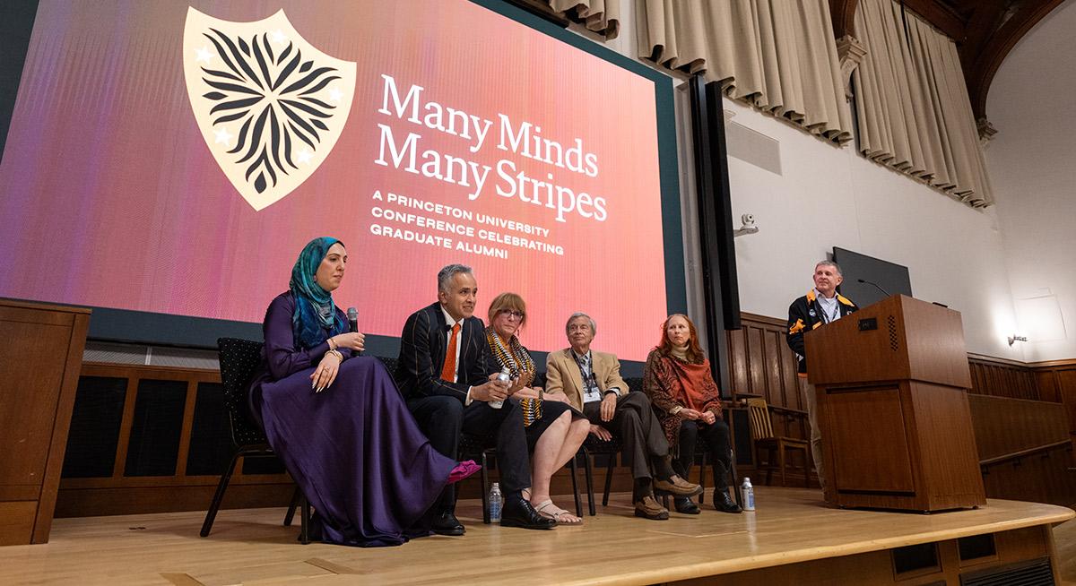 A Many Minds Many Stripes conference panel, with four alumni seated on the stage