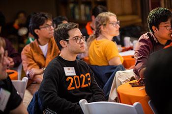 Man in a sweater saying 2023 in a room of people