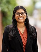 Portrait of Aishwarya Swamidurai in black jacket, orange blouse and eyeglasses.