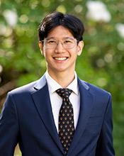 Portrait of Enzo Kho, in blue suit, black tie and eyeglasses