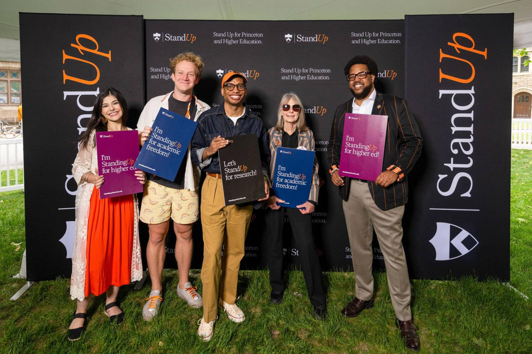 Alumni hold signs in front of Stand Up banner Alumni pose in front of the Stand Up for Princeton and Higher Education banner